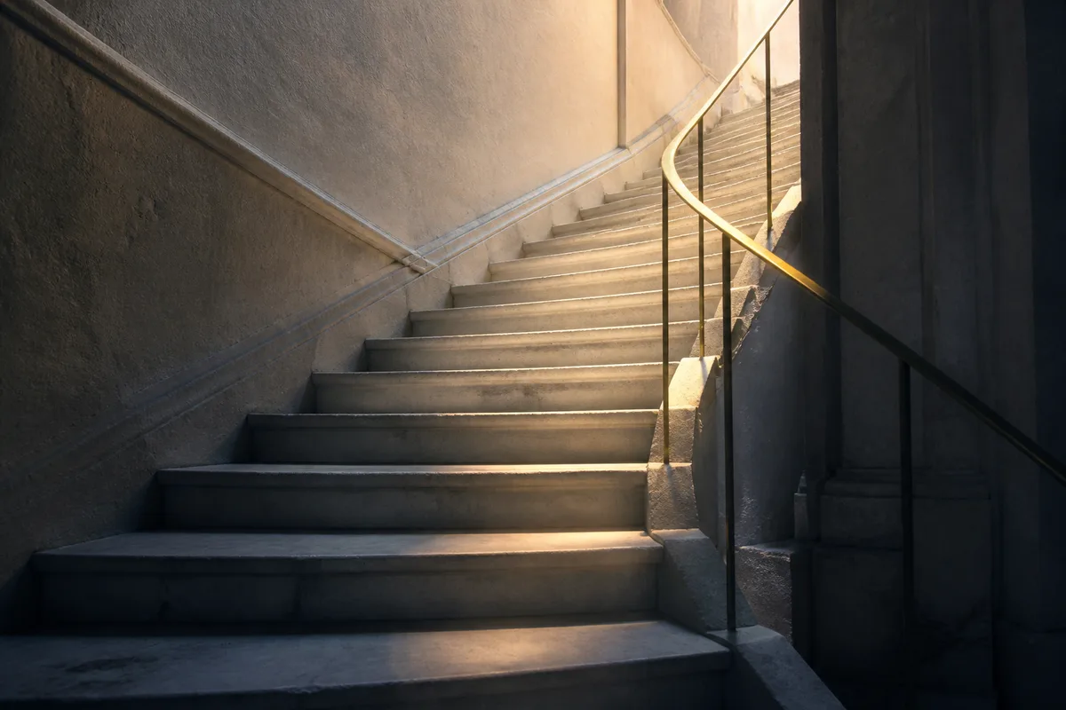 Escalier intérieur en pierre claire éclairé par une lumière latérale montante
