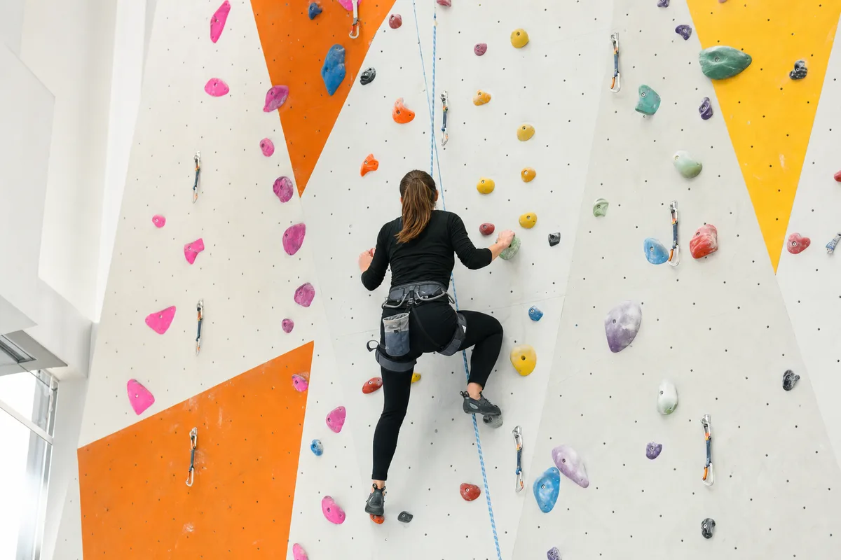 Personne de dos sur un mur d’escalade en salle avec corde de sécurité, image du défi calibré sans panique